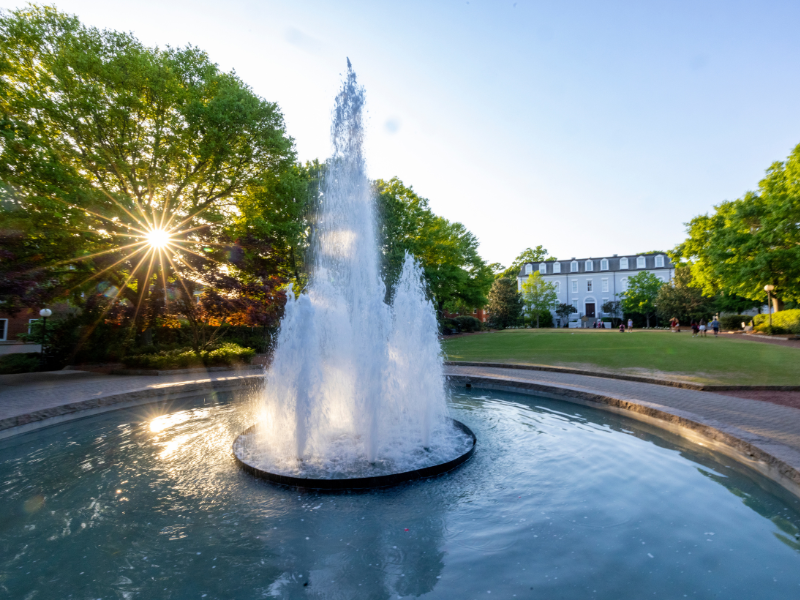 Late afternoon view of the Herty Field fountain with the sun filtering through the trees and reflecting off the water.